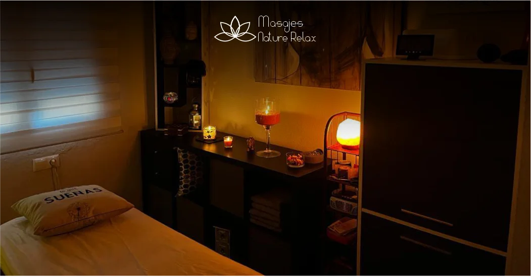 Sala de masajes, con una cama de color blanco y muchas velas amarillas.